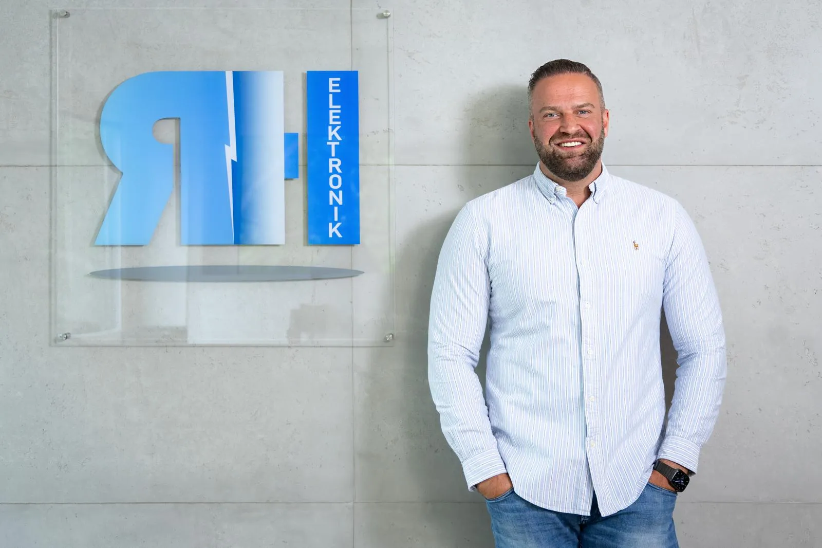 Geschäftsführer der RH Elektronik GmbH vor der Logotafel im Empfangsbereich